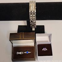 Photo showing the Guess silver tone watch on display stand next to two jewelry boxes each containing rings