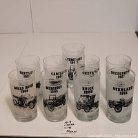 Photo of 7 of the 9 vintage frosted glasses featuring illustrations of old cars and brand/model names with years