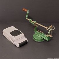 Apple peeler machine with suction base and wooden handle, displayed alongside the cherry pitter closed in compact form.