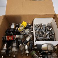 Wide view of a cardboard box filled with multiple electron tubes of various sizes including boxed and loose tubes