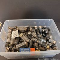 Clear plastic bin filled with numerous assorted vintage vacuum tubes and some packaging showing brand names
