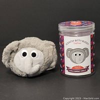 Gray plush elephant Bitty Buddy and the scented jar shown side by side against dark background.