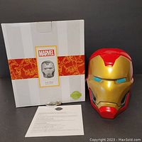 Photo of the Iron Man themed warmer next to the box, bulb, and instruction sheet showing front helmet design.