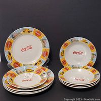 Set arranged showing four large plates in a stack, four large bowls in a stack, and one side plate with colorful vintage Coca-Cola themed borders and red central logos