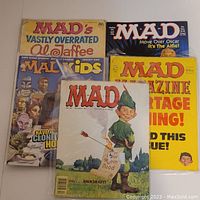 Seven vintage Mad Magazine and Mad Kids comic books arranged in a spread, showing front covers. Covers show unique satirical art featuring Alfred E. Neuman and other caricatures, with bright colors and dated titles from 1981 to 2009.