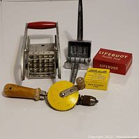 Photo capturing all tools and items in the lot arranged on a white surface, showing potato cutter, ice crusher, hand drill, Lifebuoy box, and bobbin.