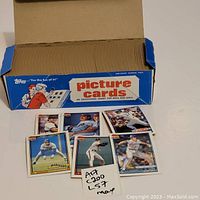 View of several baseball cards in front of open vending pack box showing 7 individual cards laid out in front of the box.
