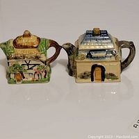 Front view of two cottage-shaped teapots showing design details and size.