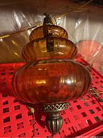Amber glass swag light lamp resting on a red crate, showing the full bulbous shape and metal top finial