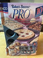 Box front showing brand Baker's Secret PRO and 10 piece set with image of various pans including pie and cake pans.