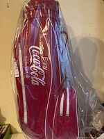 Full side profile of red Coca-Cola golf bag showing logo and plastic wrapping.