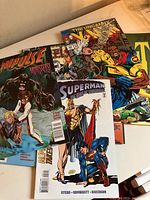 Photo showing comic books including Impulse, The Uncanny X-Men, Superman: The Man of Tomorrow, and others stacked on a flat surface.