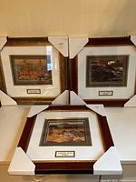 Three framed art prints with autumn scenes by Franklin Carmichael, H Mabel May, and A.Y. Jackson, displayed together with protective corner covers on the frames.