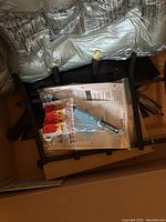 Open box showing burner assembly, hardware bag, instruction manual, and sand embers