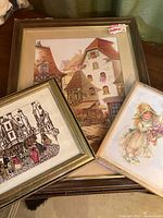 Three different framed prints overlapped showing a European street scene, vintage street crowd sketch, and girl with flowers illustration