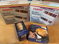Two original boxed Starfrit spice racks, plus boxed Star Basic pepper mill pump and boxed Star Basic food anchor set on wood surface
