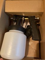 Paint sprayer gun and white paint container inside a cardboard box.