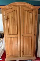 Front view of closed pine cabinet with arched top and two doors.