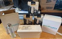 Photo shows five boxed PUR water filter faucet units, two boxes of Green Life Water bottles, five clear glass water bottles, and a white Ice Caddy container on a wooden surface.