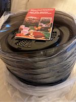 Stack of black plastic trays with clear cover, wrapped in plastic, with instruction and recipe book on top