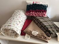 Overview of fabric rolls and trims including floral terry cloth, beige cotton, red fabric, plaid fabric, and lace-trimmed ruffles