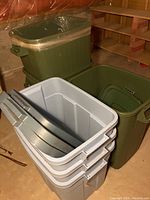 Six plastic storage totes including two green heavy-duty totes and four smaller gray totes with lids placed on the floor in basement setting.