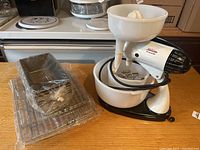 Mixer with nested large and small mixing bowls, juicer attachment on small bowl, beaters inside bowl, and power cord wrapped around mixer