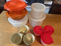 Overview of three orange vintage Tupperware bowls stacked with lids, two beige canisters with lids, two beige small condiment servers, and a red condiment server with four compartments.
