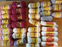 Array of assorted skeins of vintage Sayelle knitting worsted yarn arranged on wooden surface in colors burgundy, pink, white, lavender and gray.