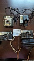 Photo of four vintage photographic items on table, including two cameras, one box camera, and one flash unit with cords.