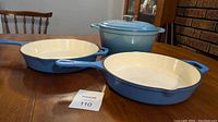 Two 16 inch blue enamel cast iron frying pans and a blue enamel cast iron stock pot on wooden table