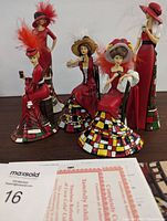 Front view showing all five Coca-Cola figurines with feathered hats and colorful dresses.