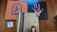 Shows three albums: The Concert for Bangladesh box with noticeable cover wear including edge damage and tear, George Harrison "Somewhere in England" album cover, and another George Harrison album with a hand and square design on cover.