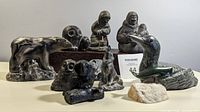 Front view of assorted 10 Indigenous sculptures including bear, owl, duck, whale, wolf, and Inuit figures on display.