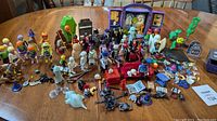 Wide layout showing all Playmobile Scooby-Doo and Halloween figures and accessories on a wooden table including multiple characters and Halloween props.