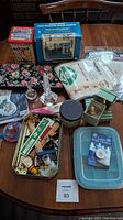 Overview of sewing machine, embroidery kits, perfume decanters, and assorted sewing notions on table