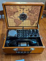 Open wooden case showing world map inside lid with compass, rotary dial, speaker, handset and control knobs on main panel.