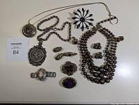 Collection of vintage jewelry items including brooches, locket pendant, necklace, earrings, bracelet, and rings laid out flat.