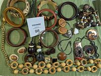 Full overview of vintage jewelry lot including multiple bangles, earrings, necklaces, brooches, and beaded belt on green cloth.