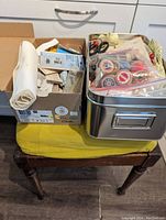 Two boxes of sewing notions and thread on top of wooden sewing bench with yellow seat cushion