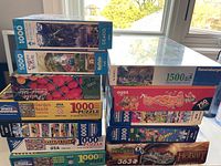 Stack of multiple jigsaw puzzle boxes showing brand, piece count and artwork.