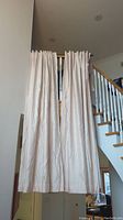 Four blush-colored blackout drapes hanging over a stair railing, showing length and light-blocking panel width. Panels appear lightly wrinkled but in good condition.