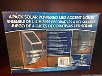 Box showing 4-pack of solar powered LED accent lights by Paradise. The box highlights stainless steel construction, two light sources, automatic lighting at night, and outdoor safety and aesthetic benefits.