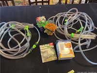 Overview of the lot on a table: two long clear irrigation hoses with green fittings, a marine aquarium manual book, replacement filter cartridge box, and a colorful artificial coral decoration piece.