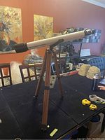 Full view of Bushnell telescope mounted on extendable wooden tripod on a table indoors.