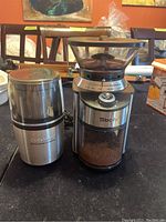 Both grinders shown side by side on a table, Cuisinart on left, Sboly on right with coffee grounds visible.
