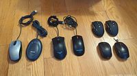 Overview photo showing 8 computer mice laid out on wooden floor, mixed wired and wireless, various brands and sizes