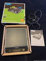 Photo shows Dymo digital postal scale in box with USB cable and instruction manual laid out beside it.
