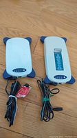 Two white and blue Energizer portable DVD batteries with attached cables on a wood floor