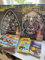 Two fuzzy posters with coloring markers, Alphabet Train puzzle, Super Balloons book, and Loomatics Rainbow Loom guide displayed on table.